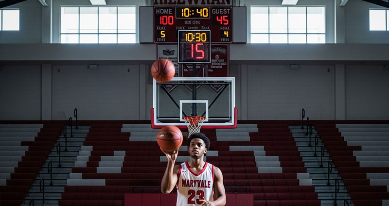 Подросток в форме баскетболиста забивает мяч в кольцо.